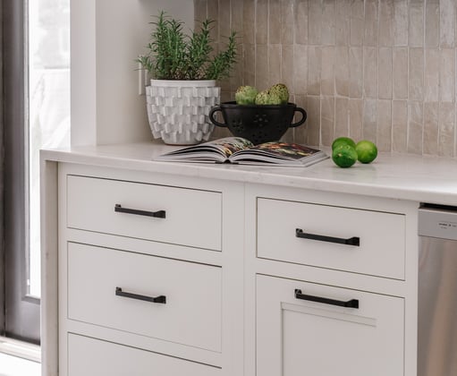 White painted cabinet drawers in a kitchen with long black handles.