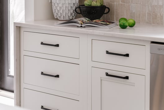Kitchen with white painted cabinets and long black handles.