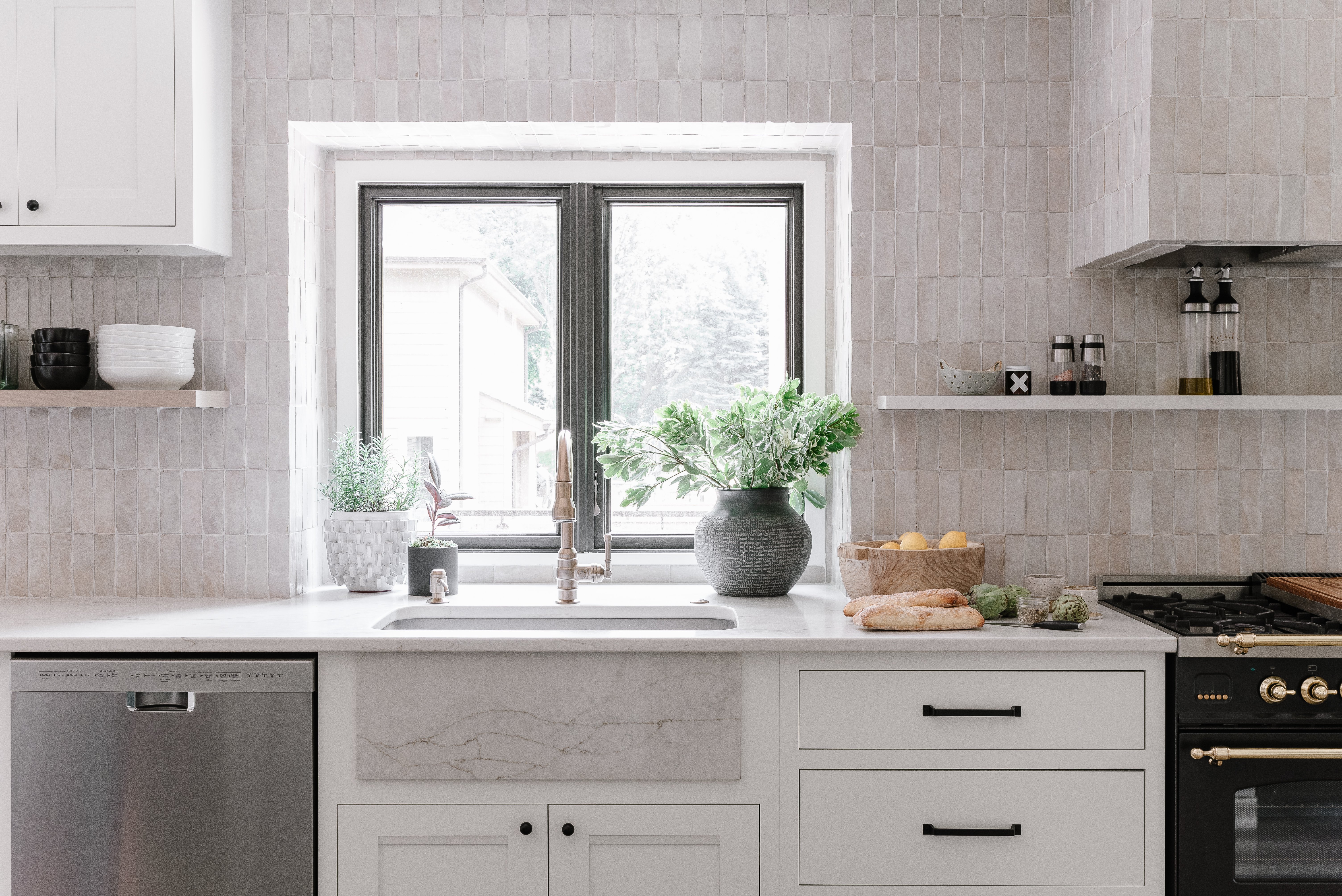 Kitchen with white painted cabinets with black handles and neutral and white backsplash, countertops and walls.