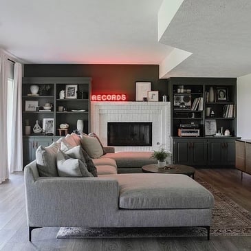 Living room with a dark accent wall and a white fireplace and a grey couch.