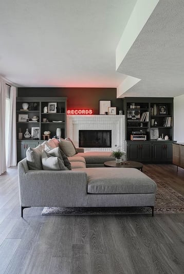 Living room with dark black accent wall with bookshelves and with a white fireplace and ceiling.