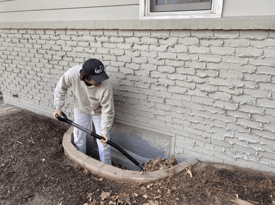 Painter cleaning out window well next to the foundation of a home in Omaha, NE.