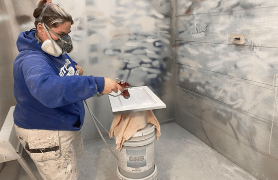 Painter spraying cabinet door white in a spray booth.