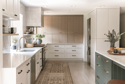 Kitchen with white cabinets and black handles and an island painted dark sage green with gold handles.