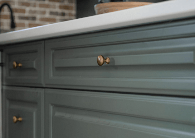 Sage green painted lower cabinets with gold knobs in a kitchen.