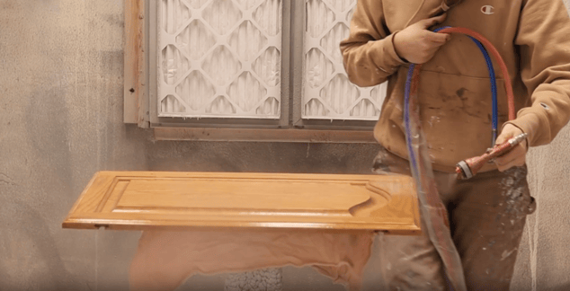 Painter spraying cabinet door with a clear coat of a polyurethane resurfacer.