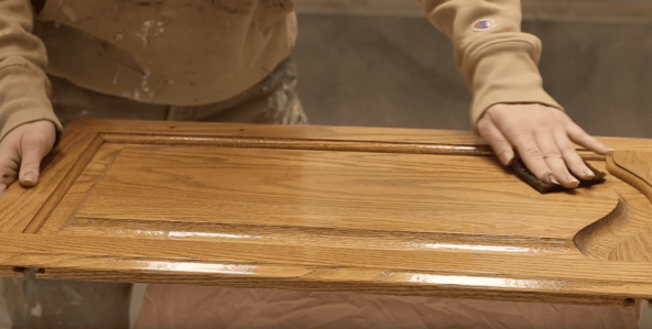 Cabinet painter cleaning golden oak cabinet door with denatured alcohol and prep pad.