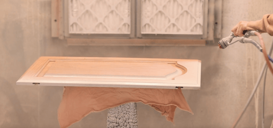 Painter spraying a golden oak cabinet door with white primer.