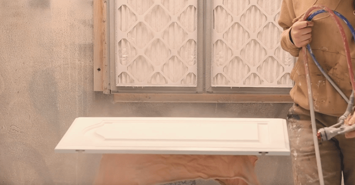 Cabinet door being sprayed white in a shop at Brush & Roll Painting.