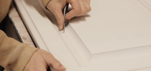 Cabinet painter using a small buff pad to smooth out an imperfection on a cabinet door.