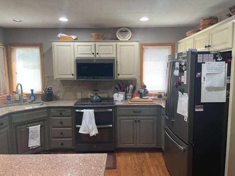 Kitchen with painted cabinets, upper cabinets are a off white and lower cabinets are a darker grey. Window trim in kitchen are natural golden oak. 