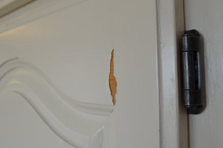 White cabinet door face that is peeling, revealing golden oak underneath.