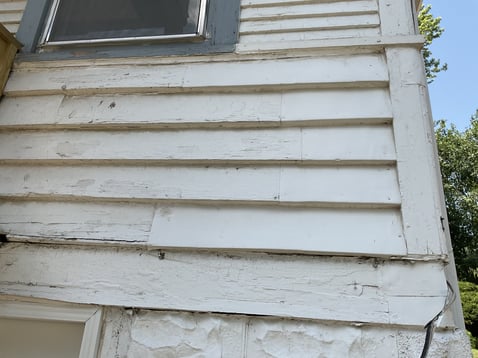 Exterior of home with damages to the off-white wooden siding.