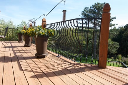 Lightly stained wooden deck with curvy iron black railings and rods.