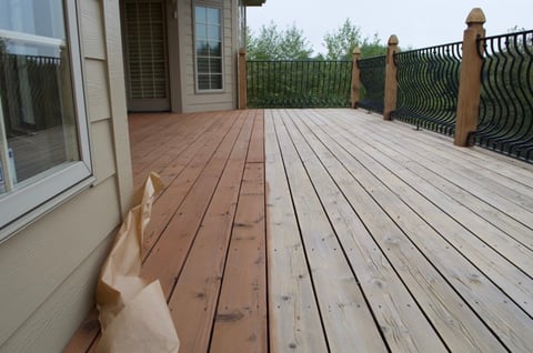 Deck boards in the middle of being stained with a warm medium toned brown deck stain.