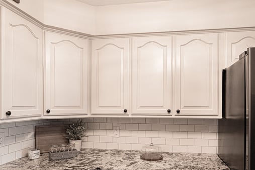 Upper white kitchen cabinets with block knobs and a granite countertop and white backsplash.