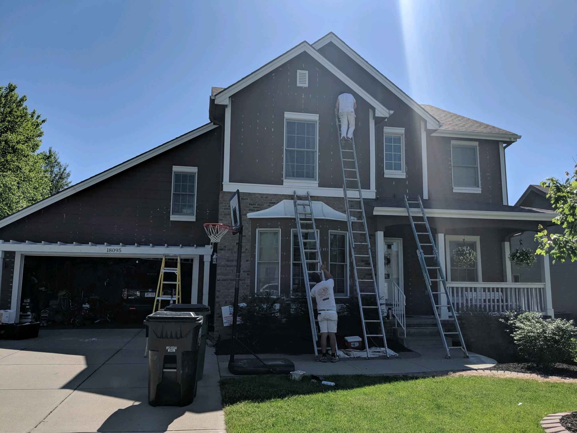Painters working on exterior of house in Omaha, NE with ladders against the side, preparing for painting.