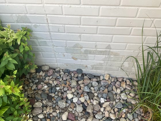 Paint peeling off of brick stone on the foundation of a home.