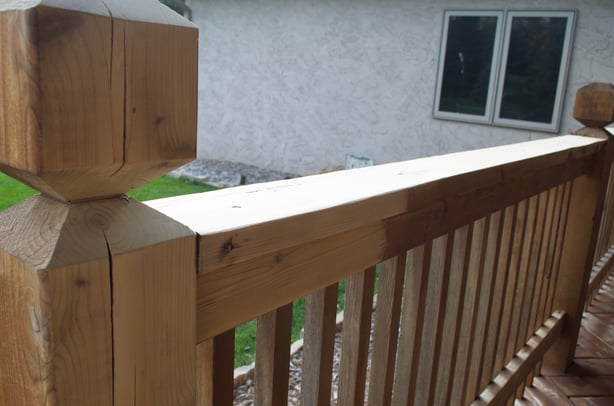 Railing of wooden deck half stained with a dark brown color.