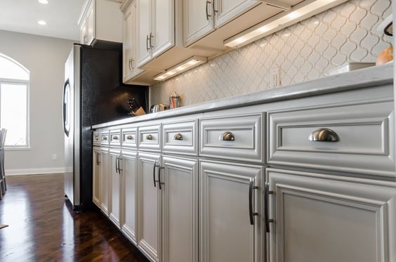 Kitchen with a wall of white cabinets with silver hardware and a fridge.