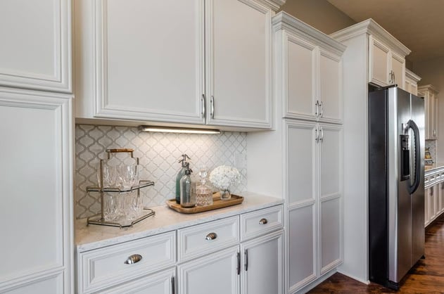 White kitchen cabinets with a white marble countertop and patterned backsplash.