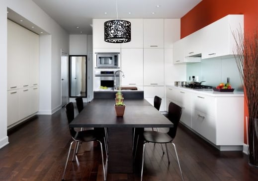 Red painted kitchen wall with white cabinets and black dining room table.