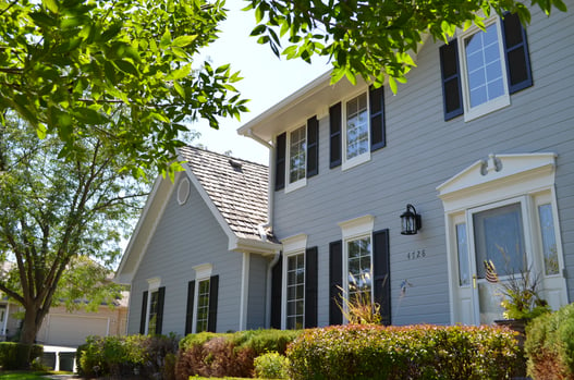 The front of the exterior of a home painted light blue with dark window shutters and white door trim.