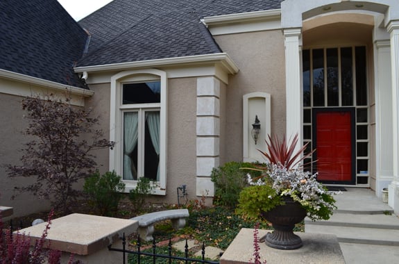 Exterior of home with light brown siding and white trim, a red front door, and dark grey roofing.