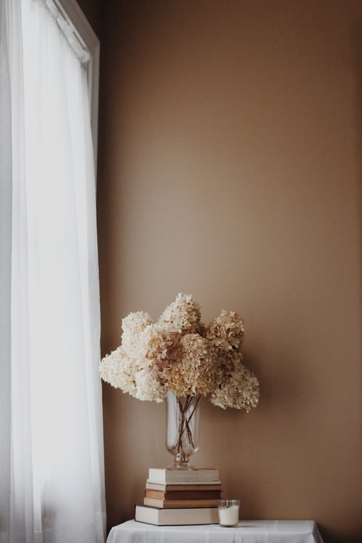 Portait of flowers in a vase on books that are stacked in front of a medium brown wall color.