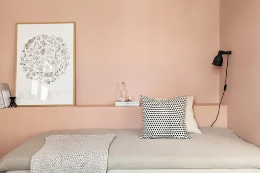 Scandinavian pink painted interior bedroom walls and a bed with neutral tan colored blanket.