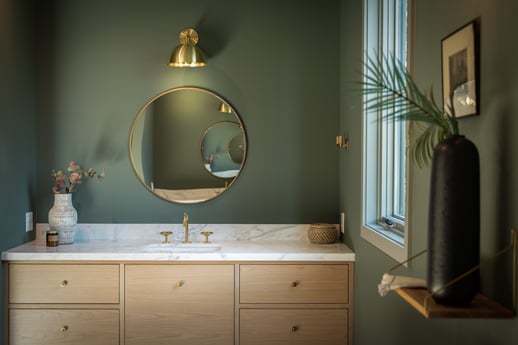 Bathroom with dark green walls, neutral vanity with white marble countertops and gold hardware.