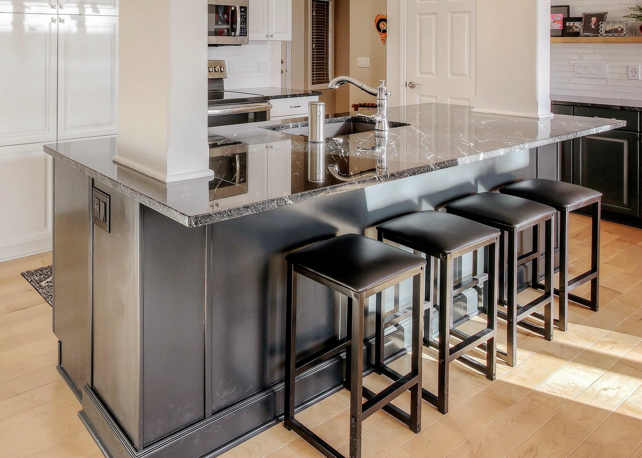 Kitchen island painted a dark brown stain with white cabinets along the wall on the lower and uppers.