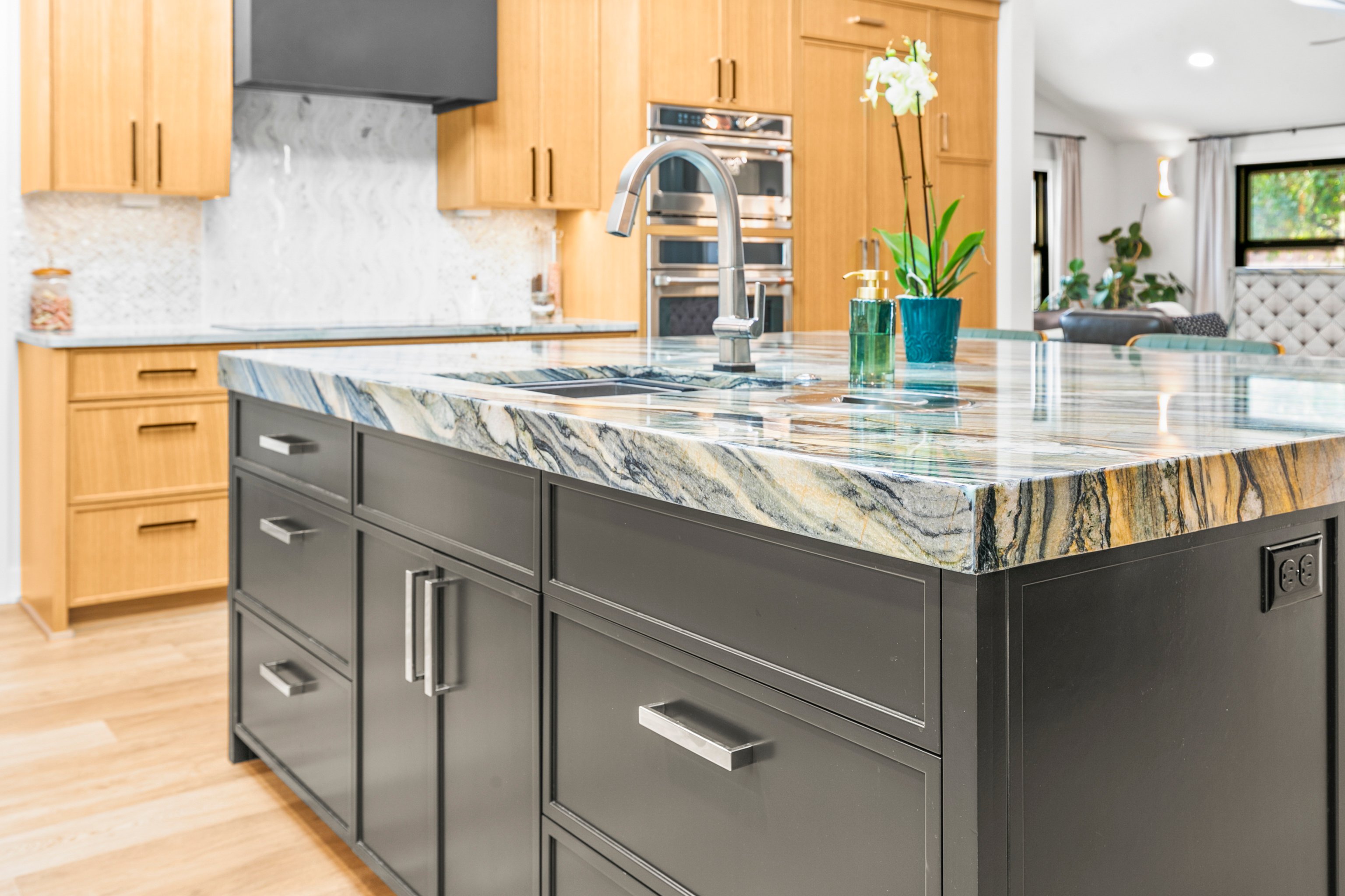 Dark colored kitchen island with warm brown cabinets in the background and a granite modern countertop.