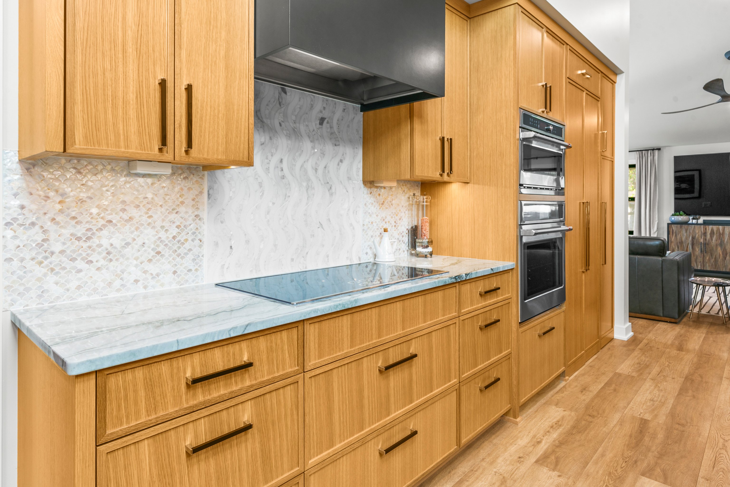 Warm wooden cabinets with white countertops and backsplash and long black pulls.