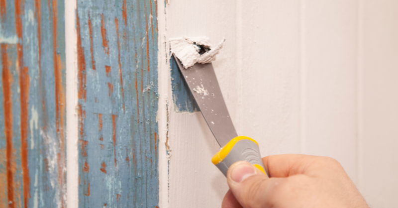 Someone scraping old paint finish off of cabinet door with a scraper.