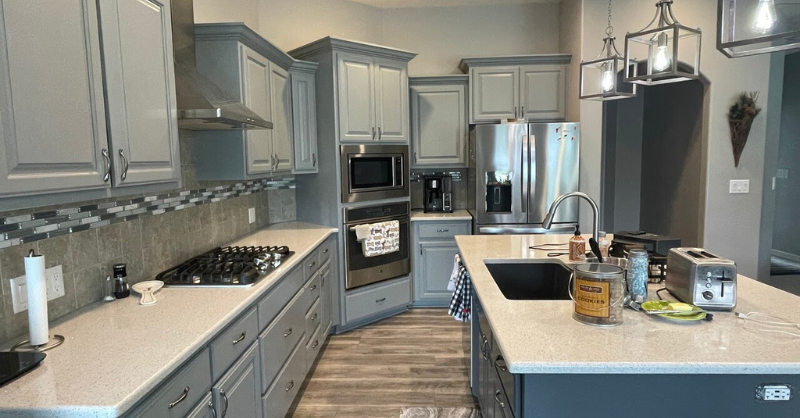Kitchen with light sage greenc abients and darker blue island and white countertops.