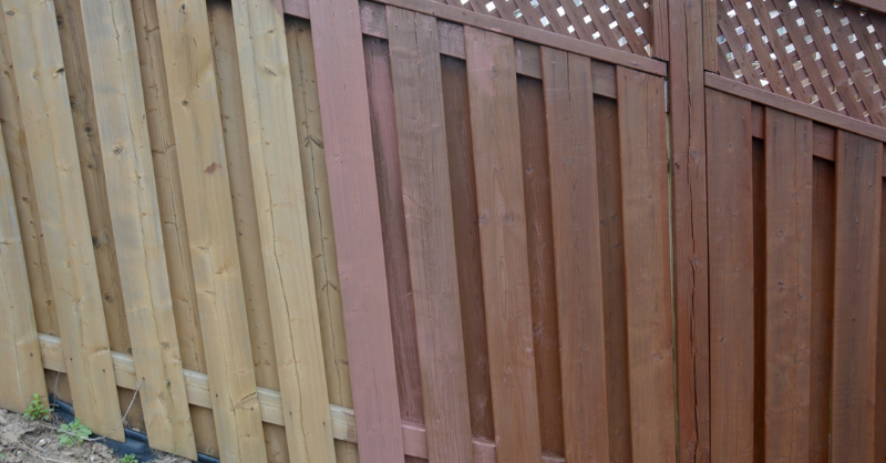 Wooden fence stained and painted various colors from bare wood to dark stain.