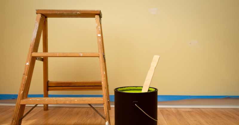 Small ladder and paint can on floor of an empty room.