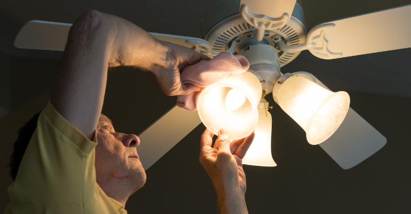 Man changing lightbulbs in ceiling fan in a bedroom.