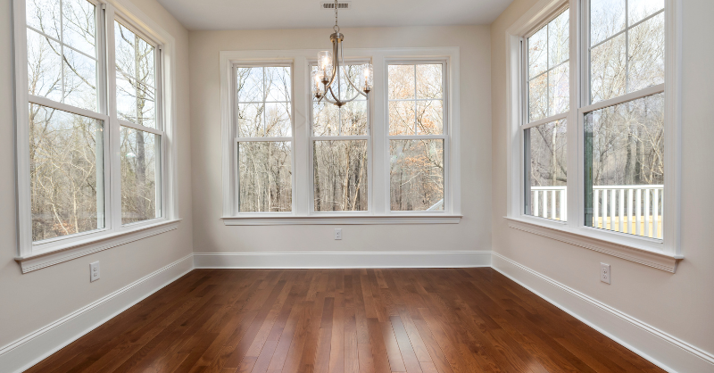Empty interior room with creamy walls and white window trim with medium brown hardwood floors.