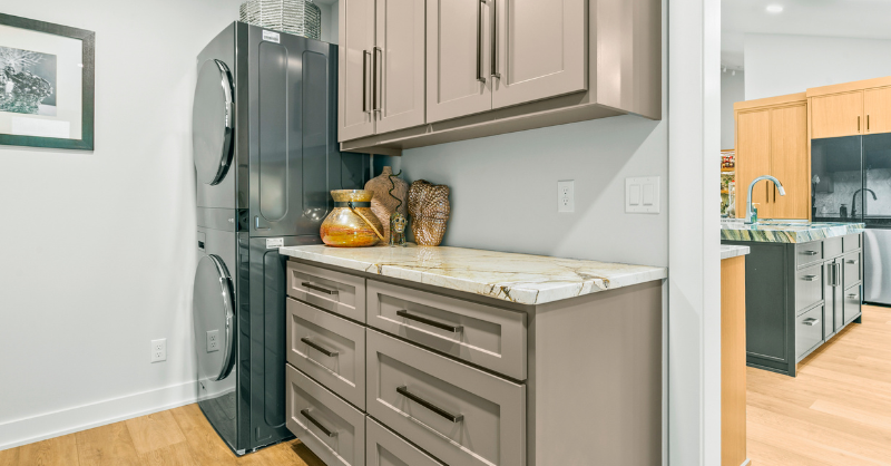 Light brown cabinet drawers and doors with a warm white countertop next to washer and dryer.