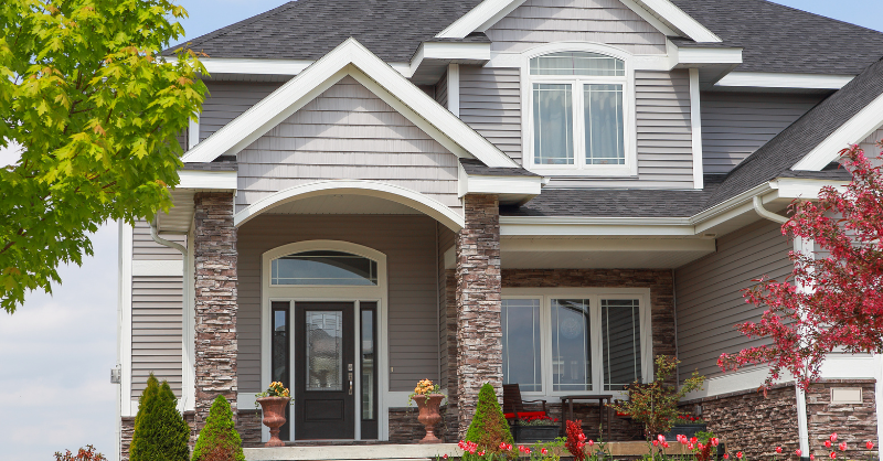 Light grey exterior of home with stone pillars and white trim.