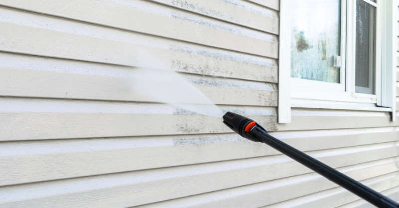 Power washer spraying dirty off white siding on home to clean it before painting.