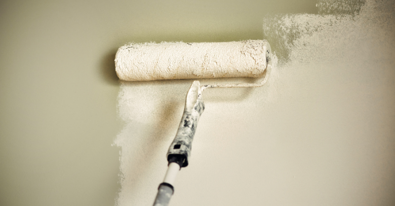 White paint being rolled onto a sage green wall.