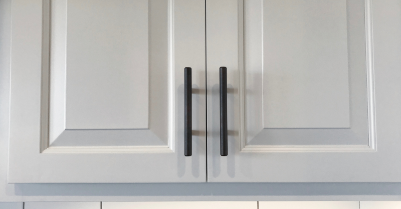 Close up image of upper cabinet doors painted white with matte black handles.