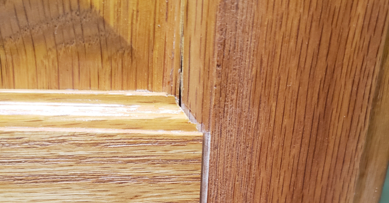 Golden oak cabinet door before staining with gaps and a crack in the wood panel.