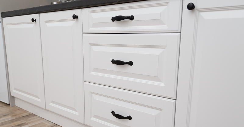 White painted cabinet doors and drawers with black handles.