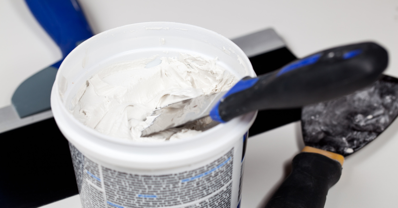 Bucket of white spackle with a scraper on the side.