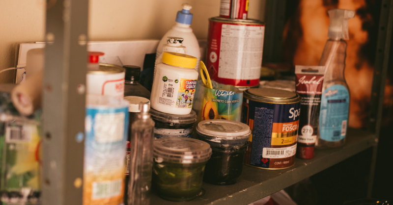 Paint cans and supplies on a shelf in a garage.