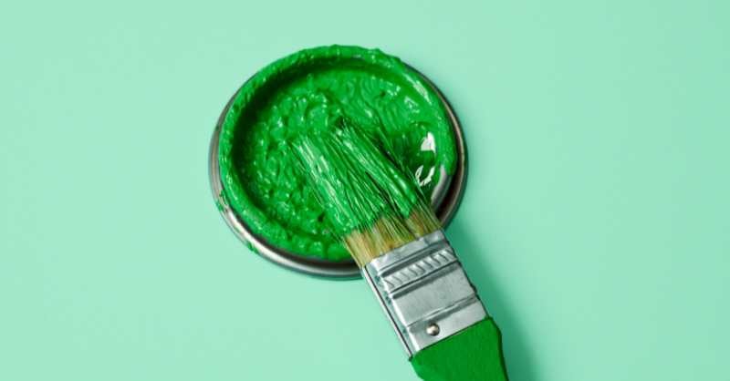 Green paint brush on top of paint can with green paint.